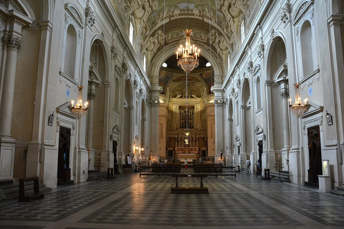 The long white nave of Santa Maria del Carmine in Florence, with tall pilasters, hanging chandeliers, a chequered stone floor and the high altar at the far end