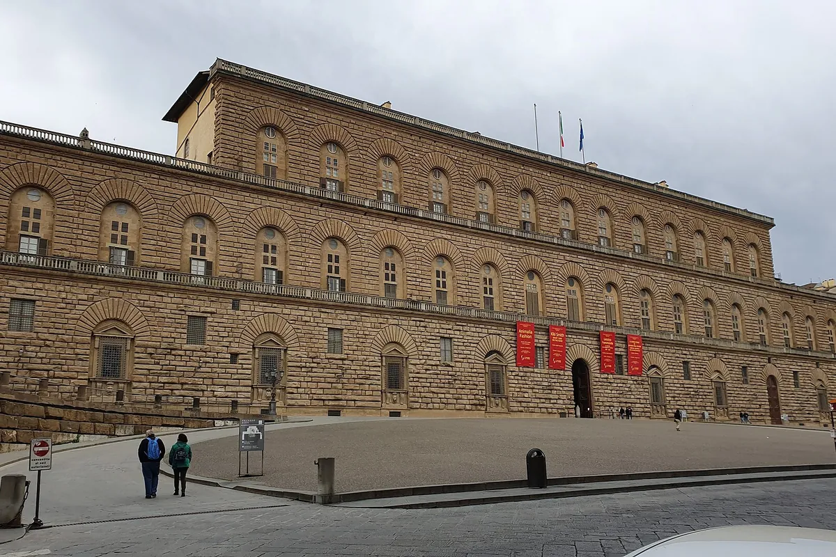 The long stone facade of Palazzo Pitti in Florence, rows of arched windows above rusticated stonework
