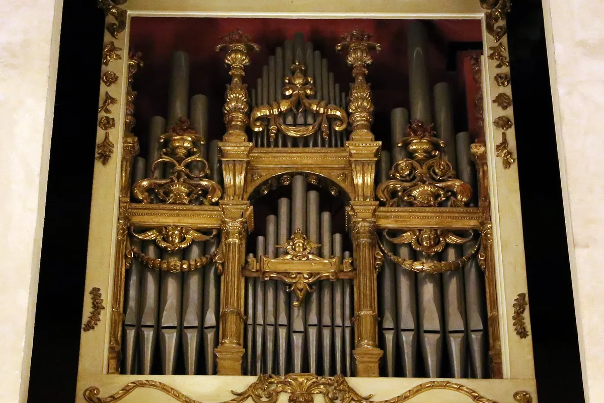 A gilded organ case with silver pipes set in a window in a plastered wall of Santa Monaca church